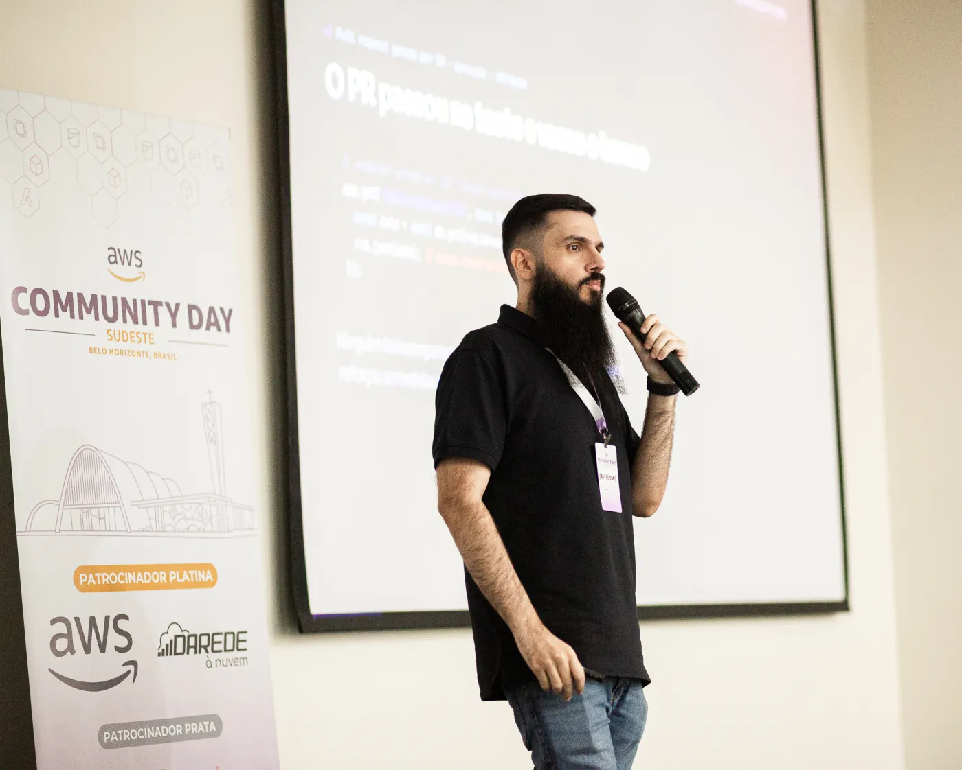 Dan Rezende no palco do AWS Community Day Sudeste, ao lado do banner do evento